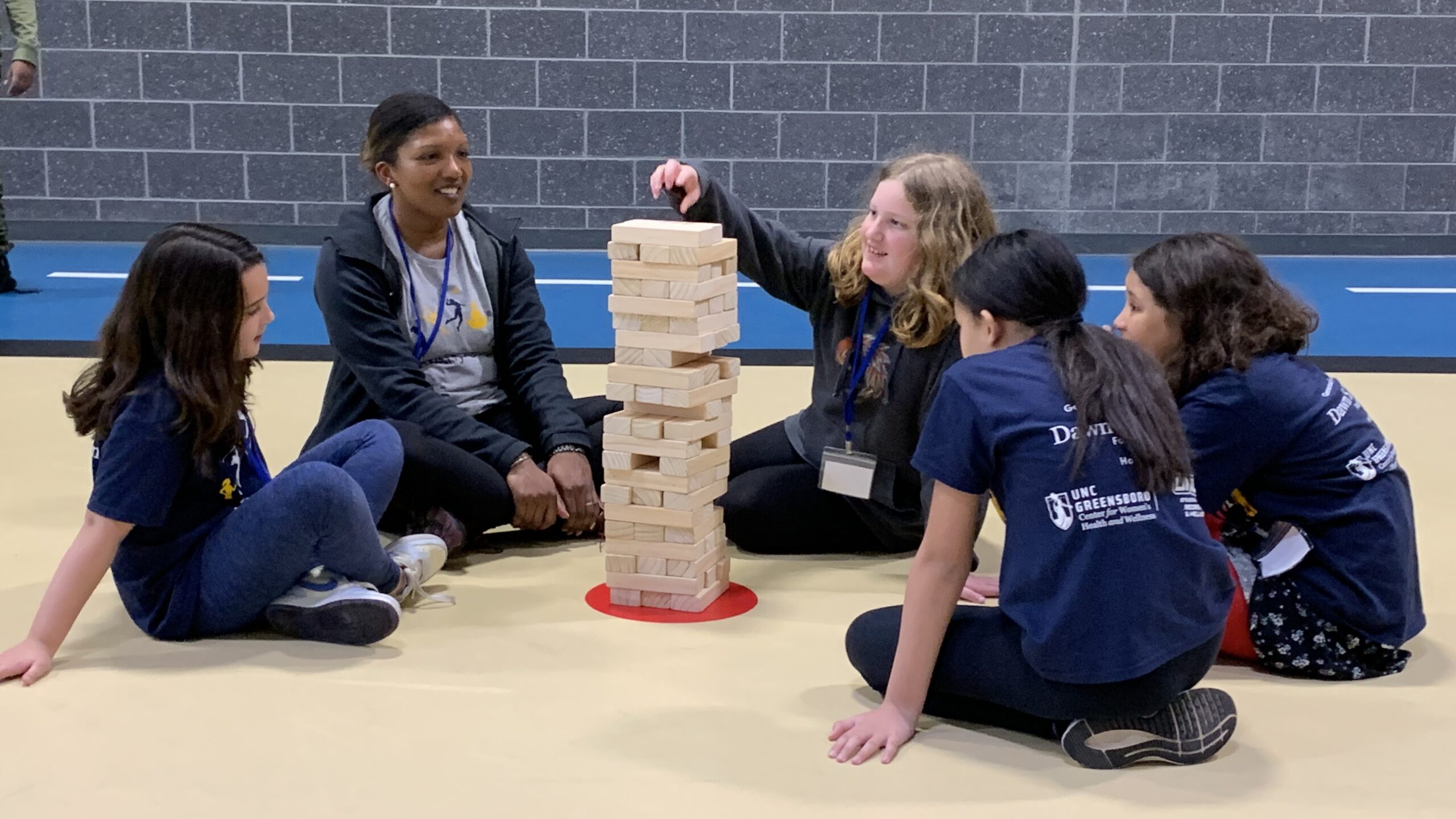 Four campers sit with a counselor on the gym floor and play giant jenga