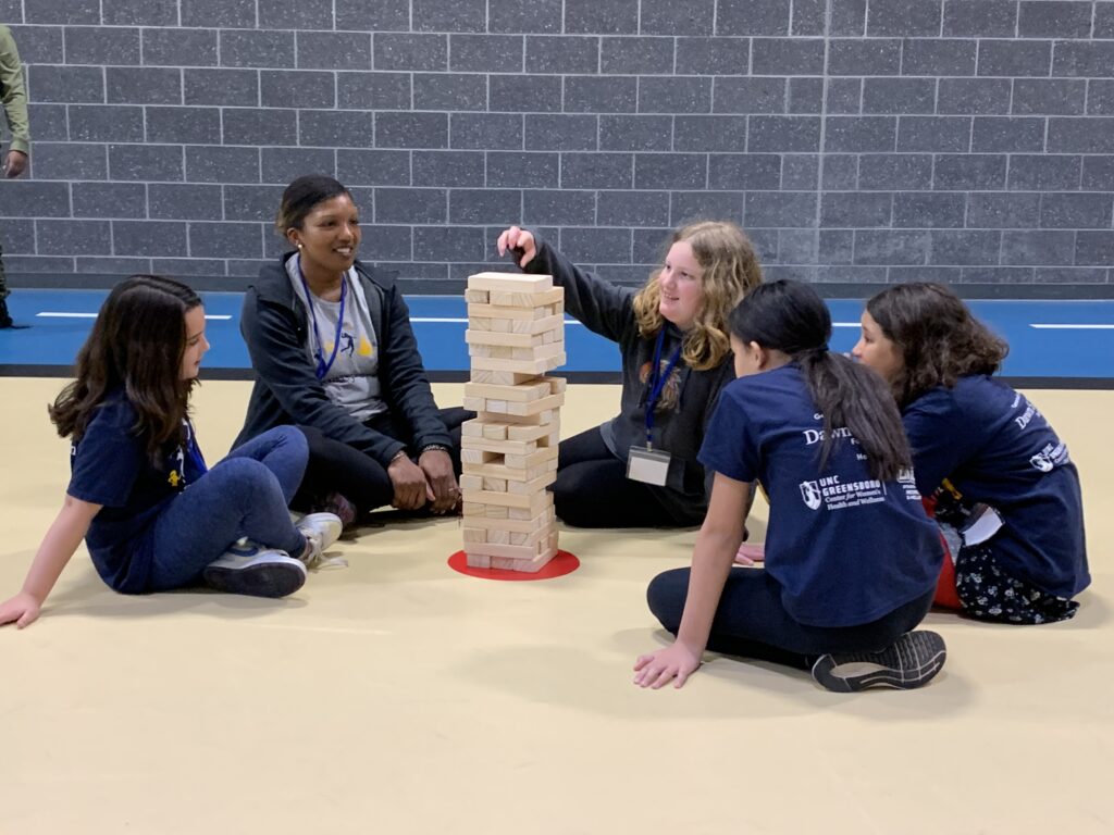 Group of campers and instructor sitting and playing giant jenga