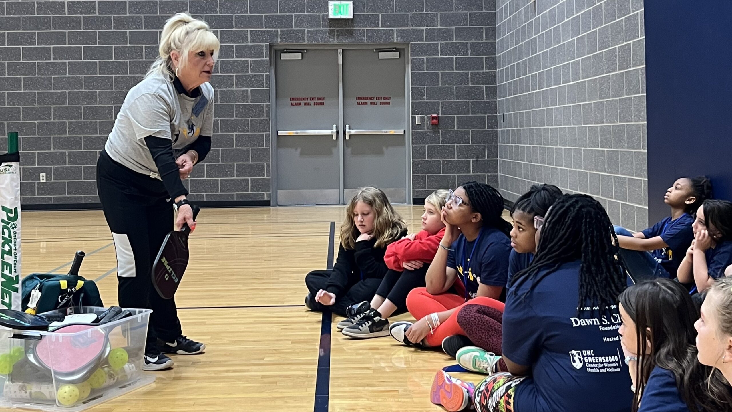 Pickleball instructor teaches a group of sitting campers how to swing the paddle